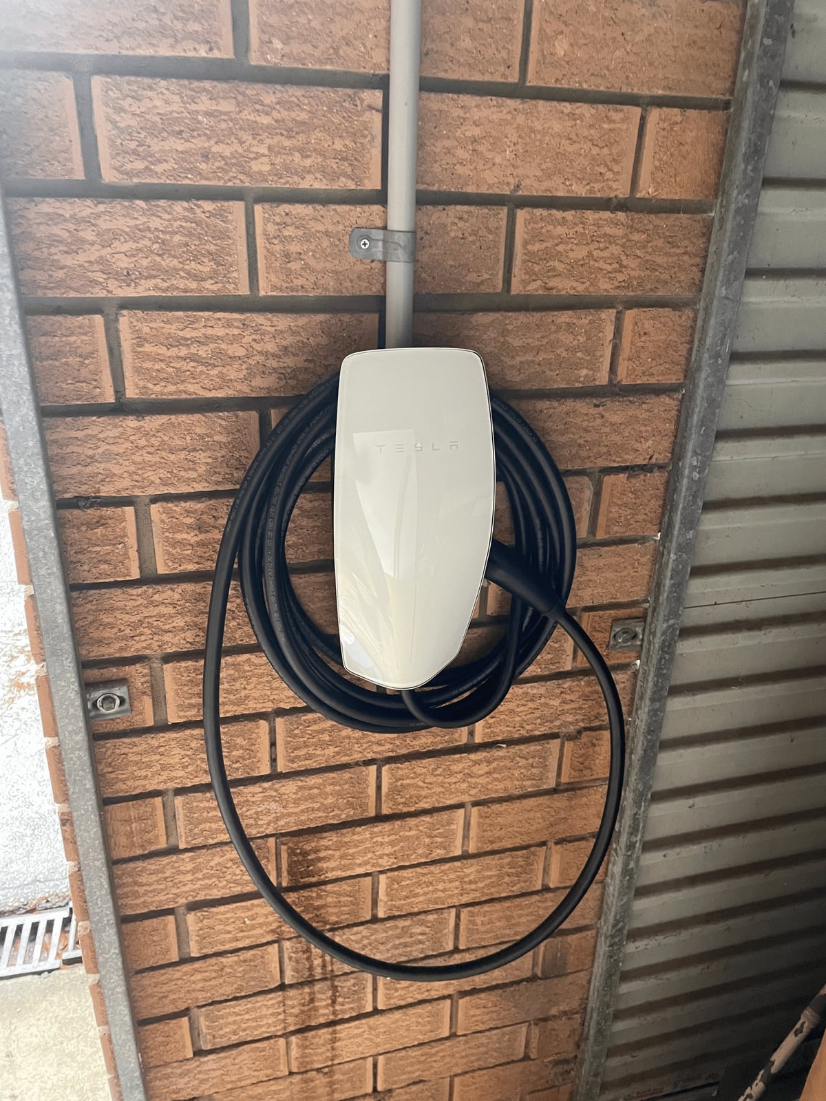 Tesla wall connector installed on a brick wall with coiled charging cable