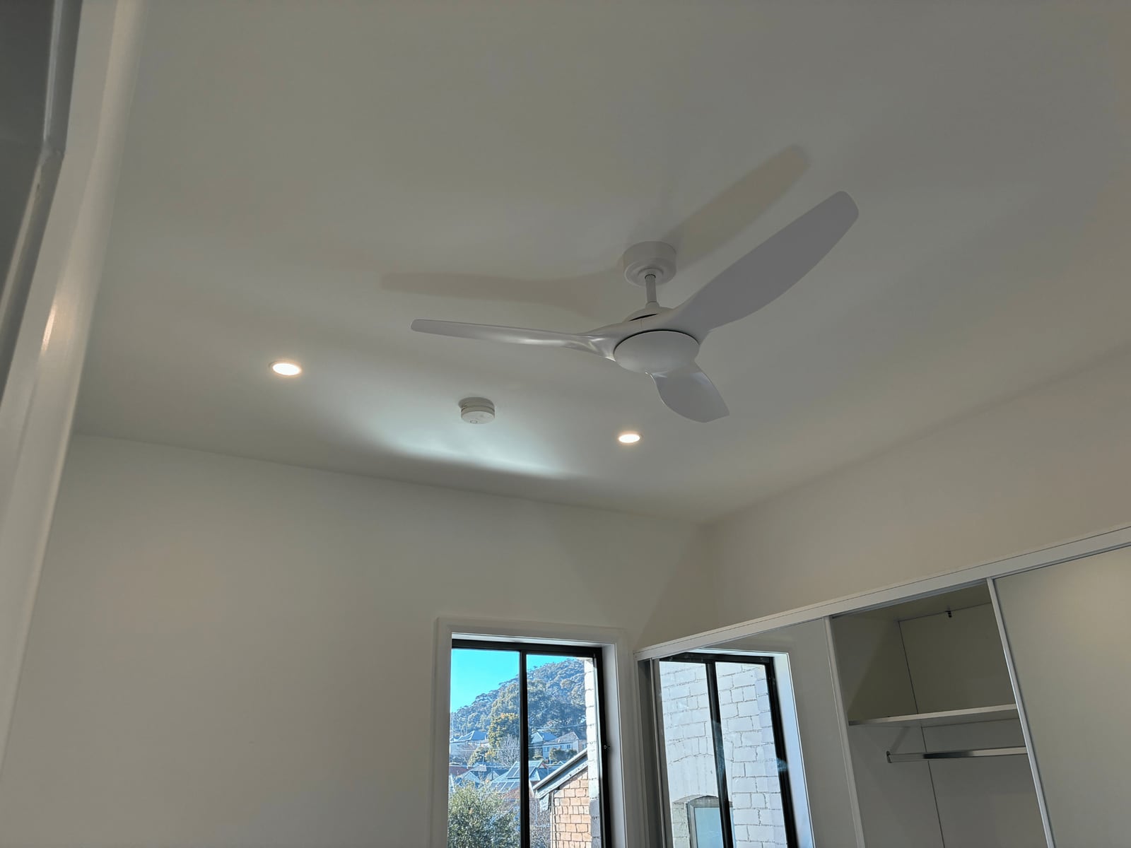 Ceiling mounted smoke alarm beside downlights and a ceiling fan